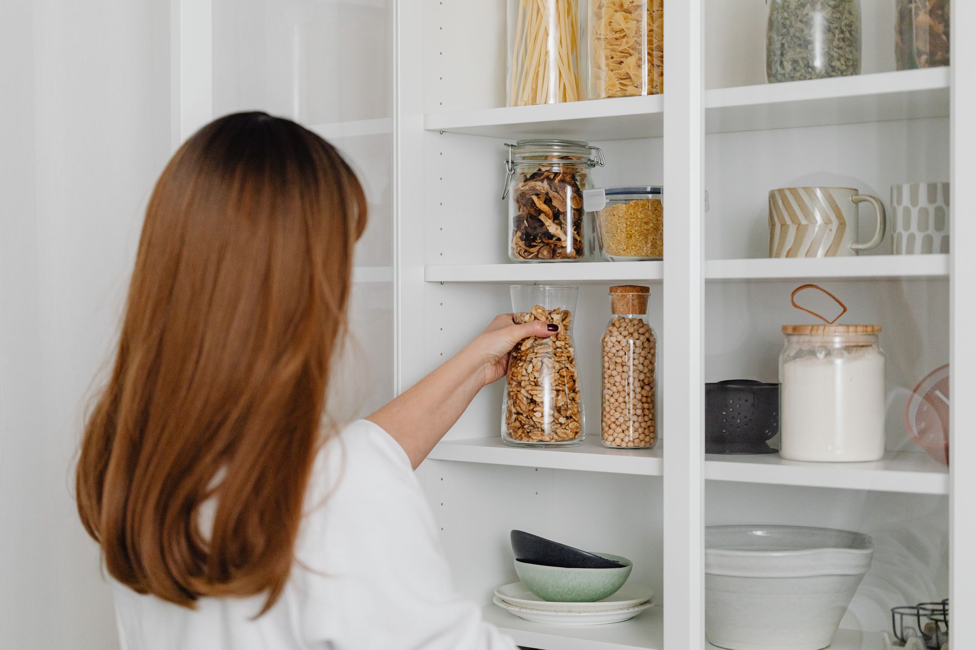 Woman in a white shirt standing in front of a kitchen cabinet and holding a glass jar