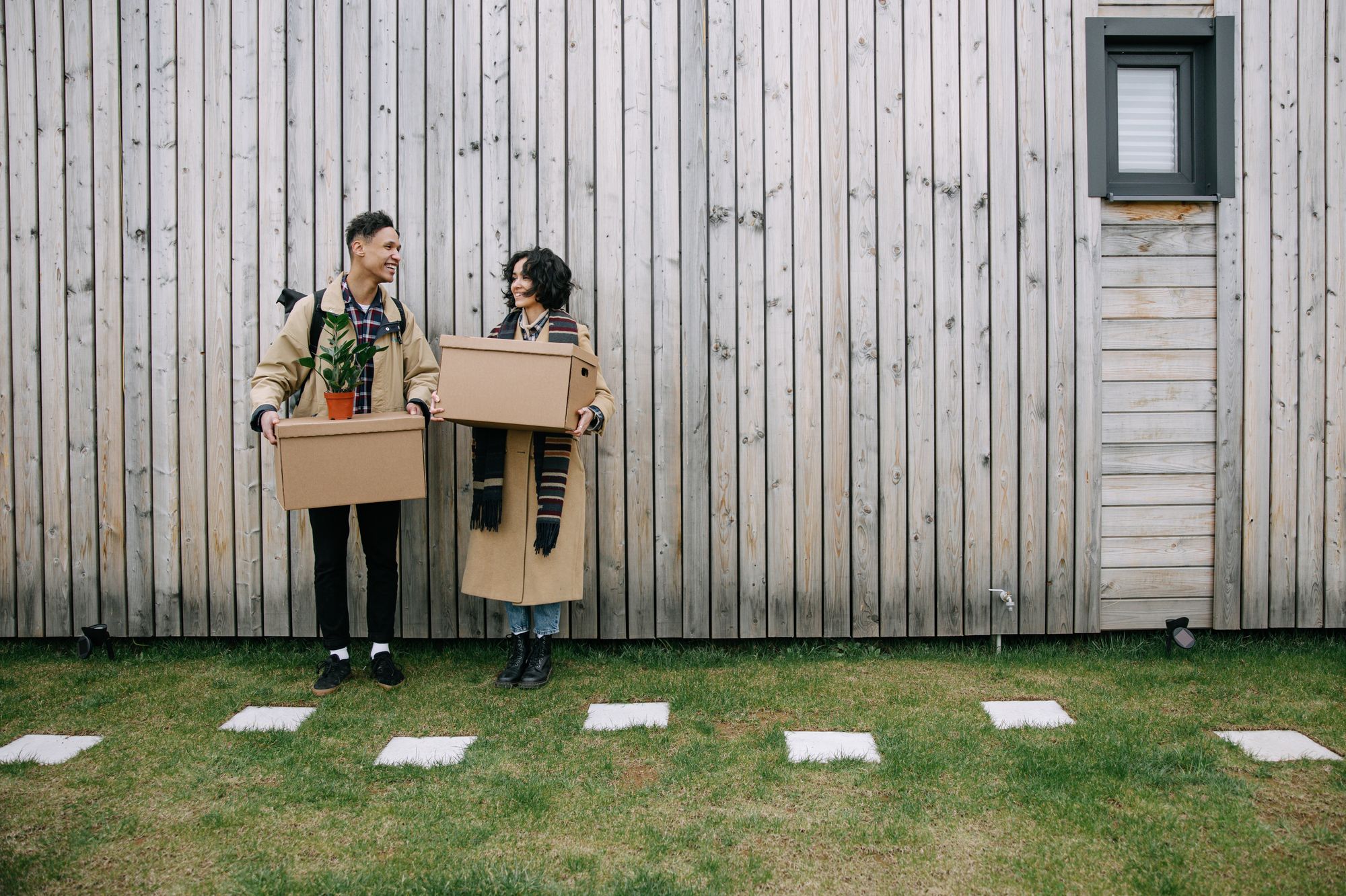 Two people holding moving boxes and standing in front of a house
