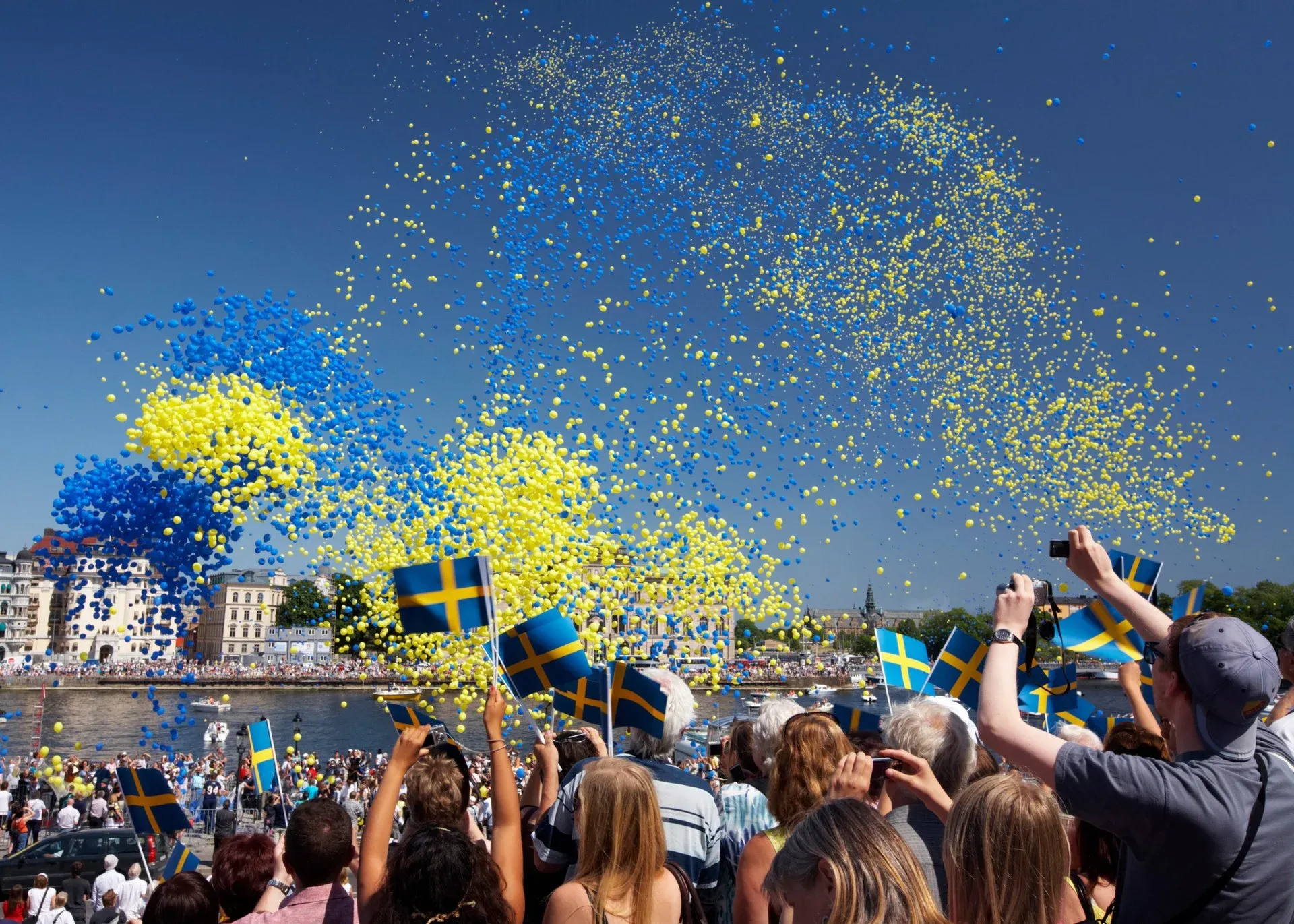 A crow of Swedes waving the Swedish flag and releasing balloons to celebrate Sweden National Day