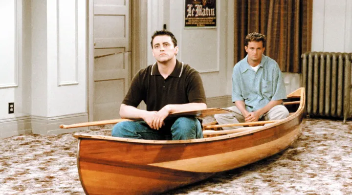 Photo from TV series F.R.I.E.N.D.S, depicting two roommates, seated in a canoe in the middle of a living room