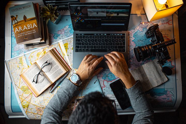 Man sitting at a table and working on a laptop, with multiple maps in the background