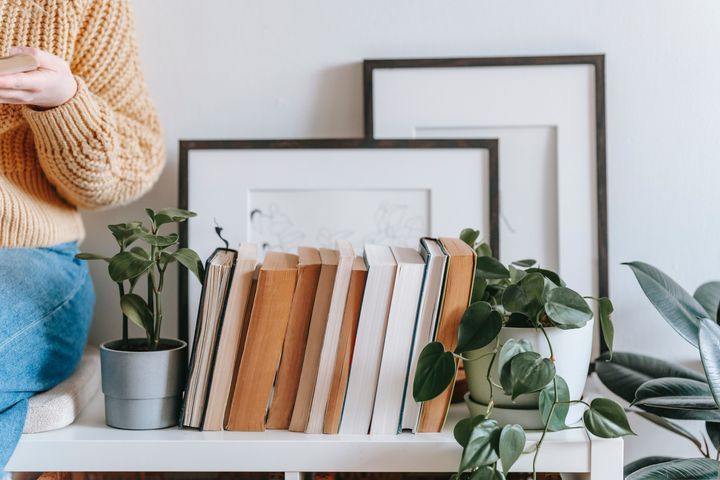 A woman sits next to a pile of books, some frames and plants