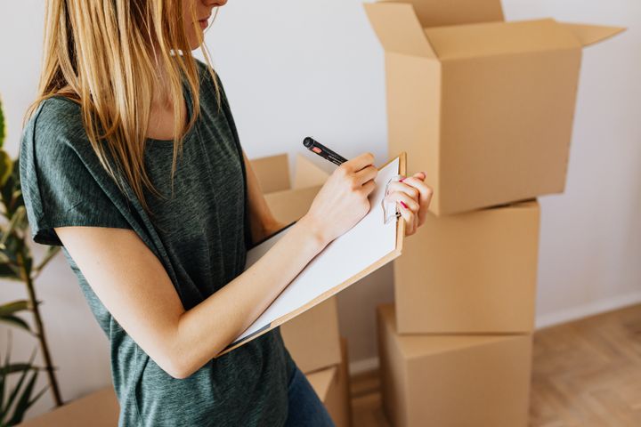 Woman taking notes on a clipboard, behind her is a pile of carton boxes