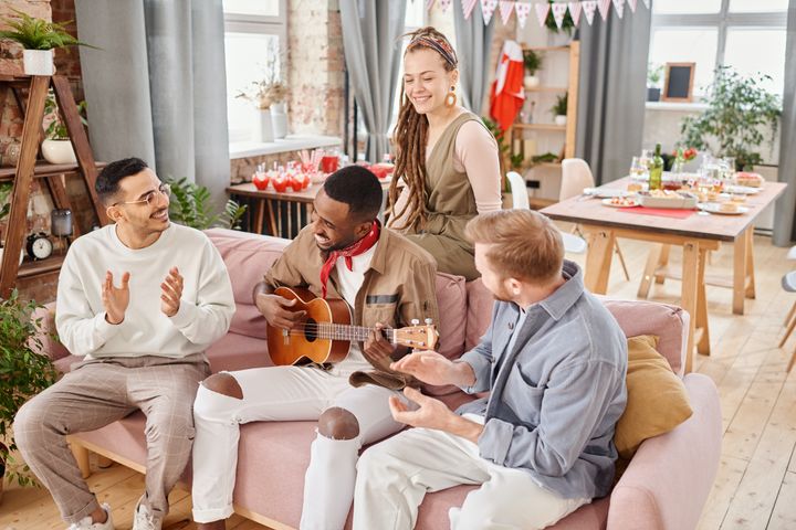 Photo of group of people sitting on a couch, a few of them are clapping while one plays the guitar