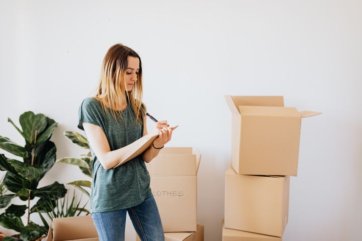 A woman writing down notes while standing in front of a pile of packing boxes