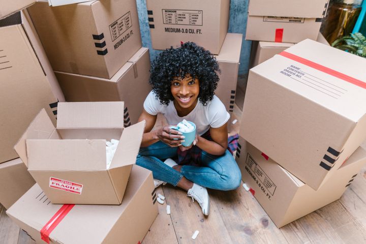 A girl in a blue shirt sitting on the floor, surrounding by a pile of moving boxes