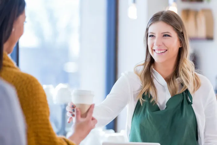 A part-time barista passes a coffee to a customer