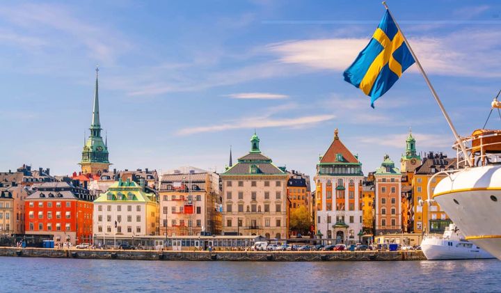 Photo of a boat with a Swedish flag, cruising in front of Stockholm's port