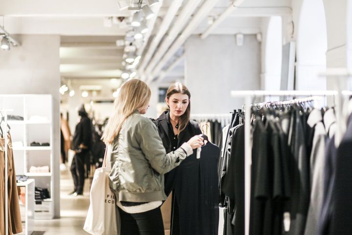 Two women standing in front of a clothes rack at a shopping store