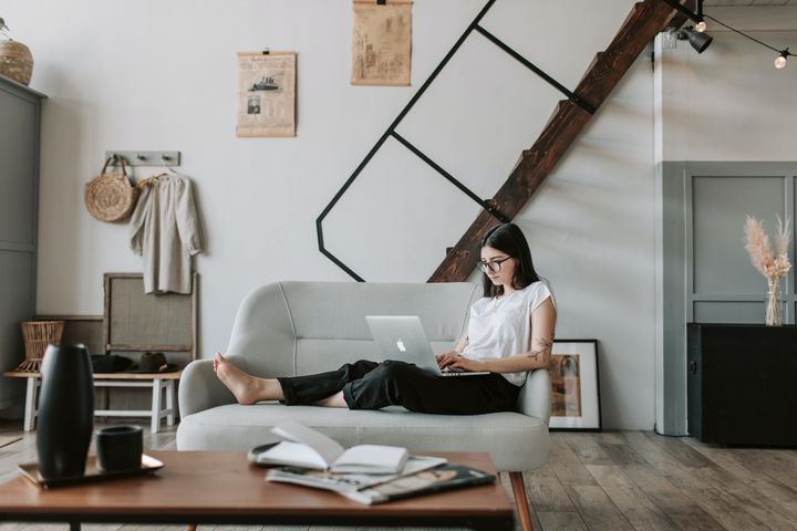 A woman sitting on a couch, working on her laptop, with a view of the entire room