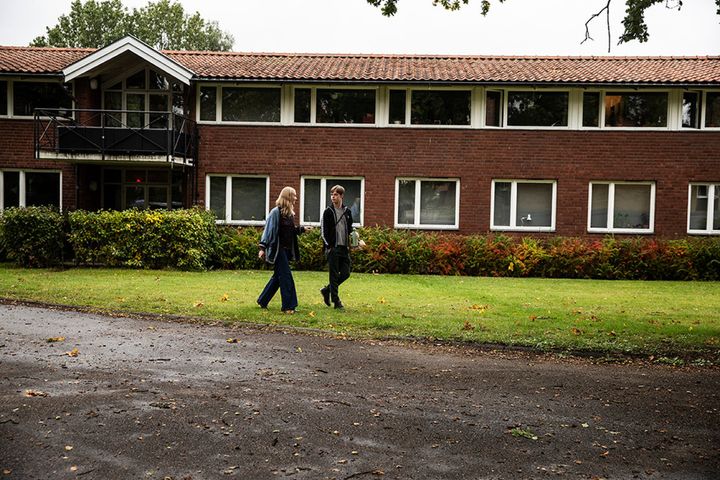 2 students walking in front of Fridhems Folkhögskola during the day.
