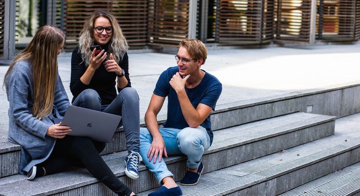 Three students seated on steps at the University of Copenhagen, one holding a laptop