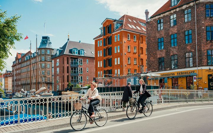 Two individuals ride on their bikes on the streets of Copenhagen in De