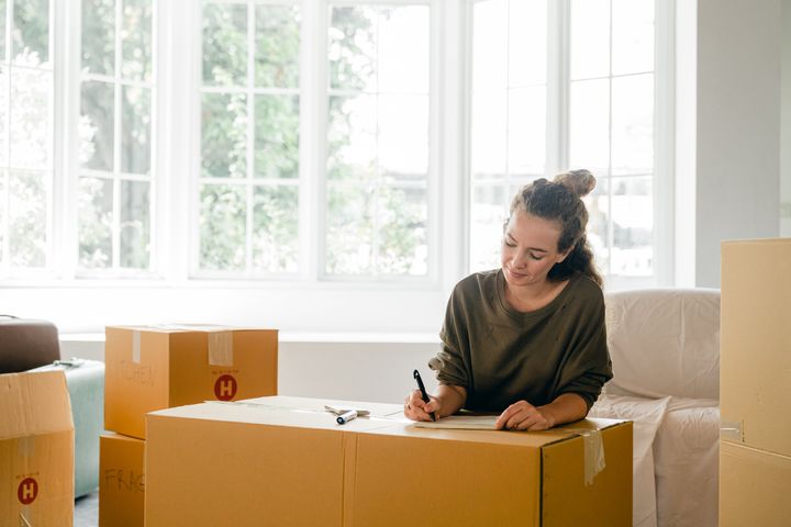 Woman signing a moving box near a large window letting in sunlight