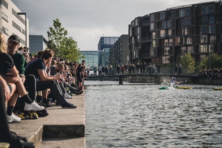 Students surround a body of water in Copenhagen, Denmark, close to a building complex of student housing