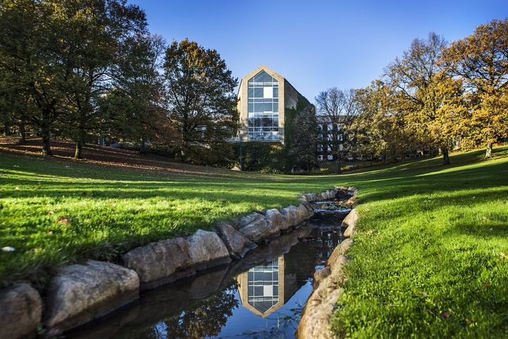 Photo of Aarhus University campus, showing lots of greenery and a small canal running across a part of campus