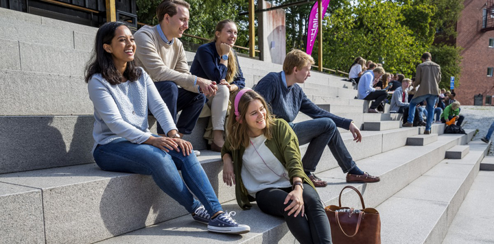 A group of students sitting on steps and smiling at a camera that's outside the frame