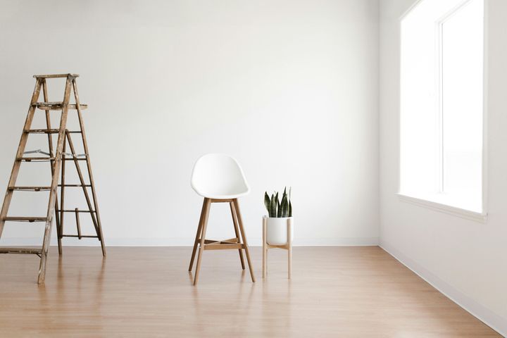 White round chair next to a vase with a plant, in an empty white room with a ladder