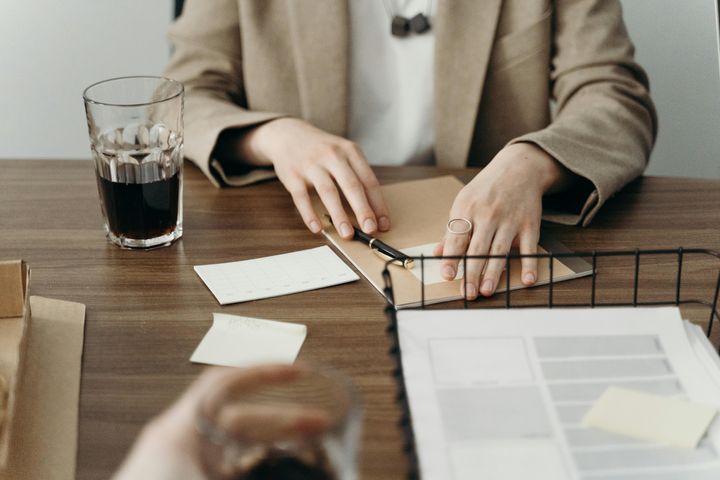 Photo of a person holding a pen, with a stack of paper in front