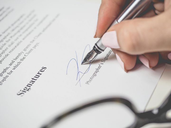 A person holding a pen and signing an agreement or a document