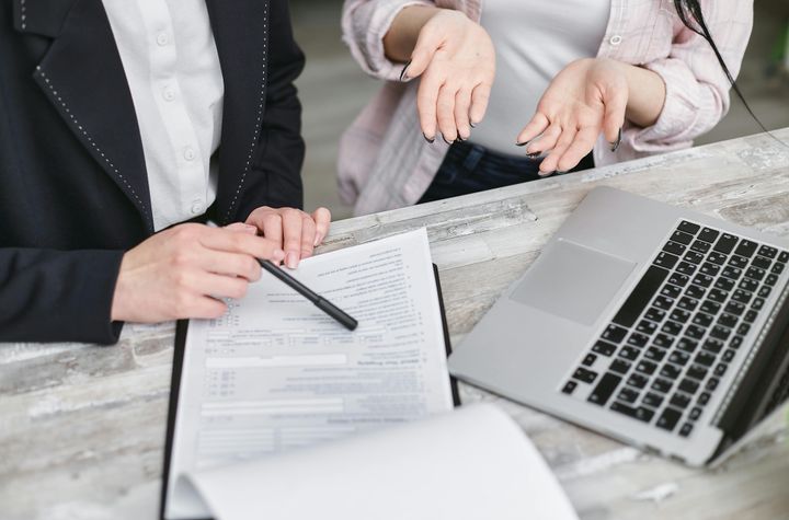 A person holding a black pen pointing at a section in an agreement, seemingly explaining it to someone