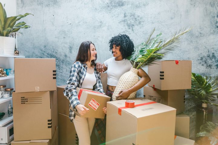 Two women surrounded by boxes and plants, seemingly moving into a new apartment