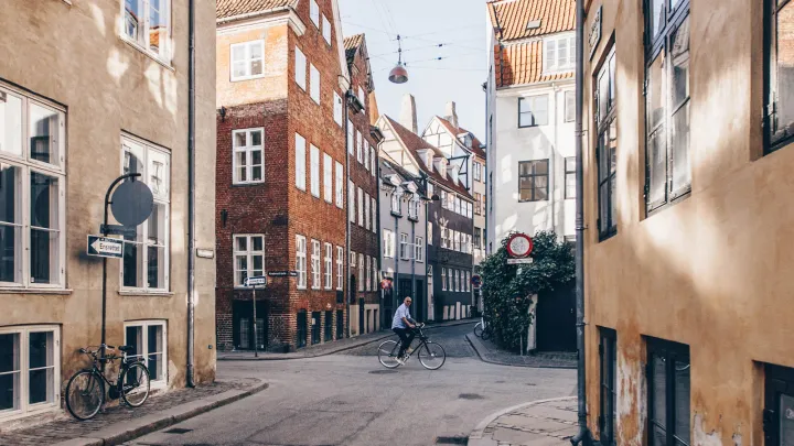 Guy riding a bike amidst several buildings in a neighborhood in Copenhagen