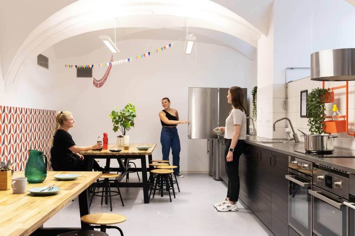 Three women standing in the kitchen of their shared apartment, seemingly talking and laughing together