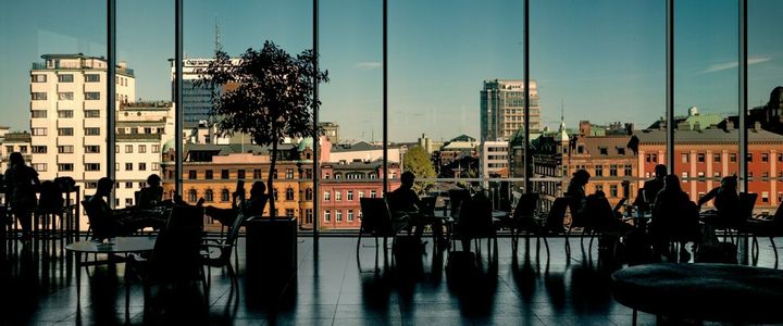 Students seated across a hall inside Malmö University, with a skyline of Malmö in the background