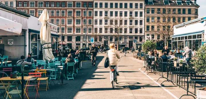 Woman riding her bike while surrounded by pedestrians and people dining in Vesterbro, Copenhagen 