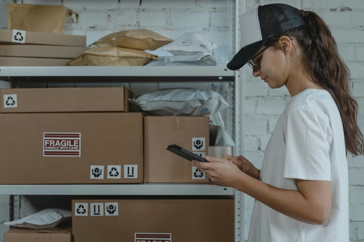 Young woman in a white shirt holding a smartphone, in front of a pile of moving boxes