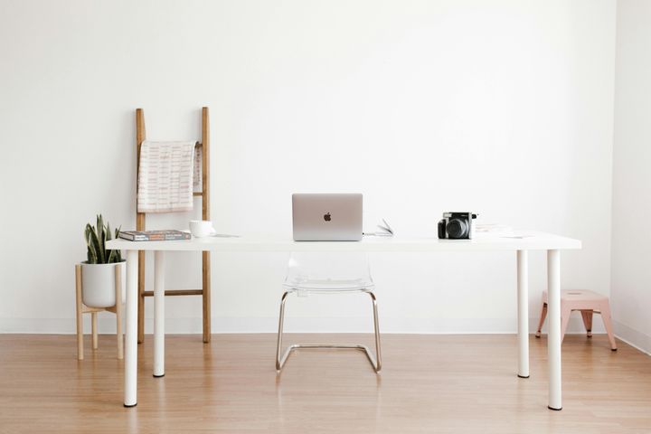 Desk with laptop and camera on top of it, with some minimal furniture in the background