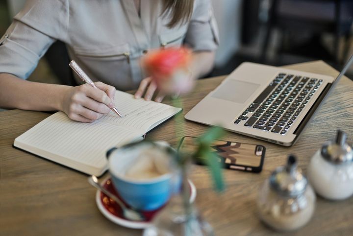 Person writing in a notebook next to a Macbook