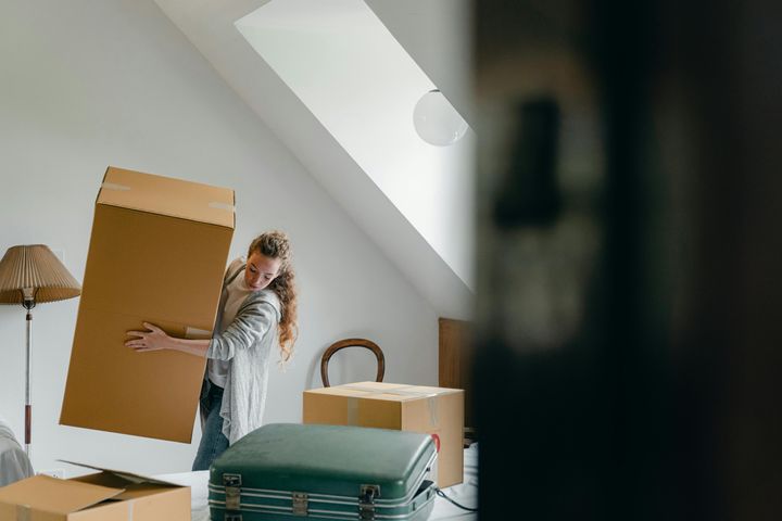 Woman carrying boxes in a new apartment, with a big suitcase in front of her