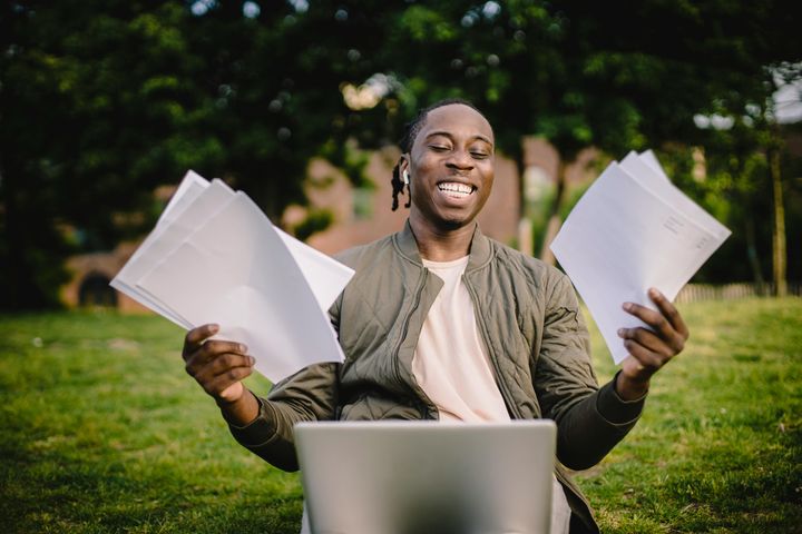 Individual with documents in both hands in front of a laptop, seemingly happy about something