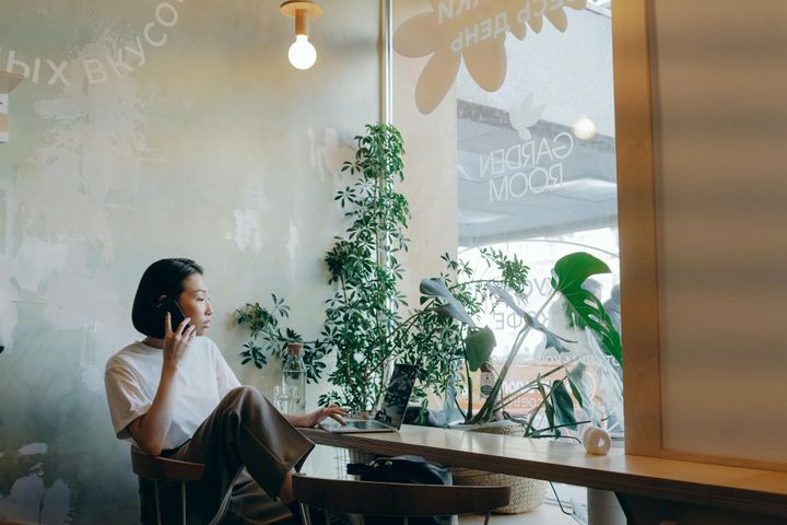 Woman wearing a white shirt, sitting on a chair in front of her laptop and speaking on the phone