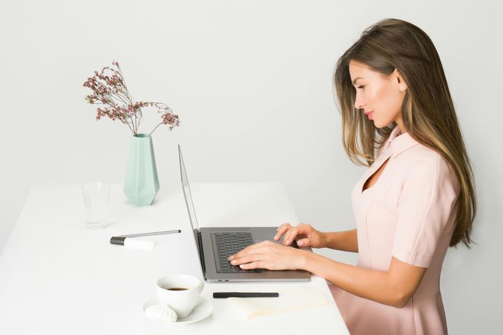 Woman in a pink dress working on her laptop at a desk