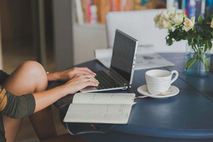 Person using a laptop, set on a table next to a notebook and a coffee mug