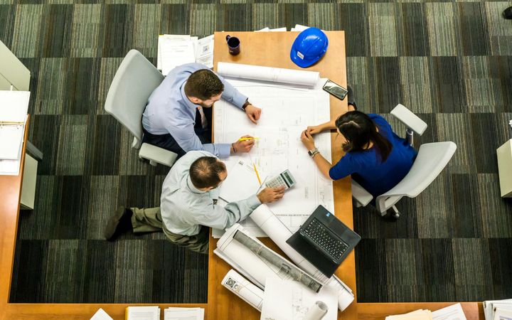 Three people looking at a large drawing of a building, on a table at work