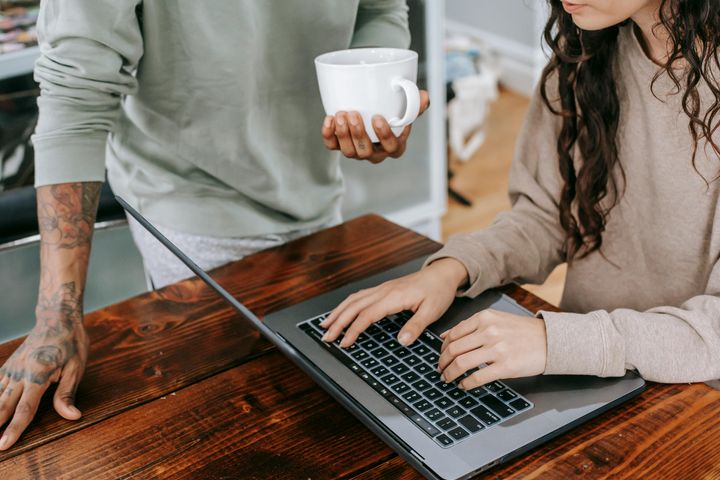 Woman typing on a laptop and a man standing next to her with a cup of coffee