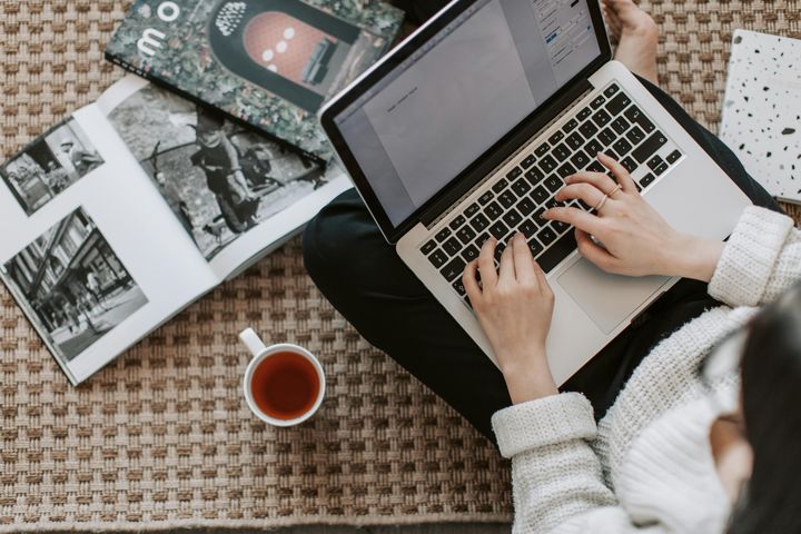 Young businesswoman working on her laptop, surrounded by magazines, with a coffee cup next to her lap